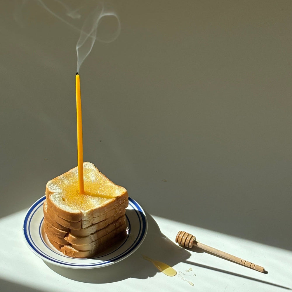 Beeswax taper candle for celebrations on a stack of wonder bread with honey.