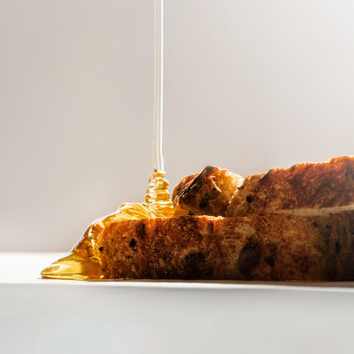 Honey being drizzled onto a piece of toast with a white background