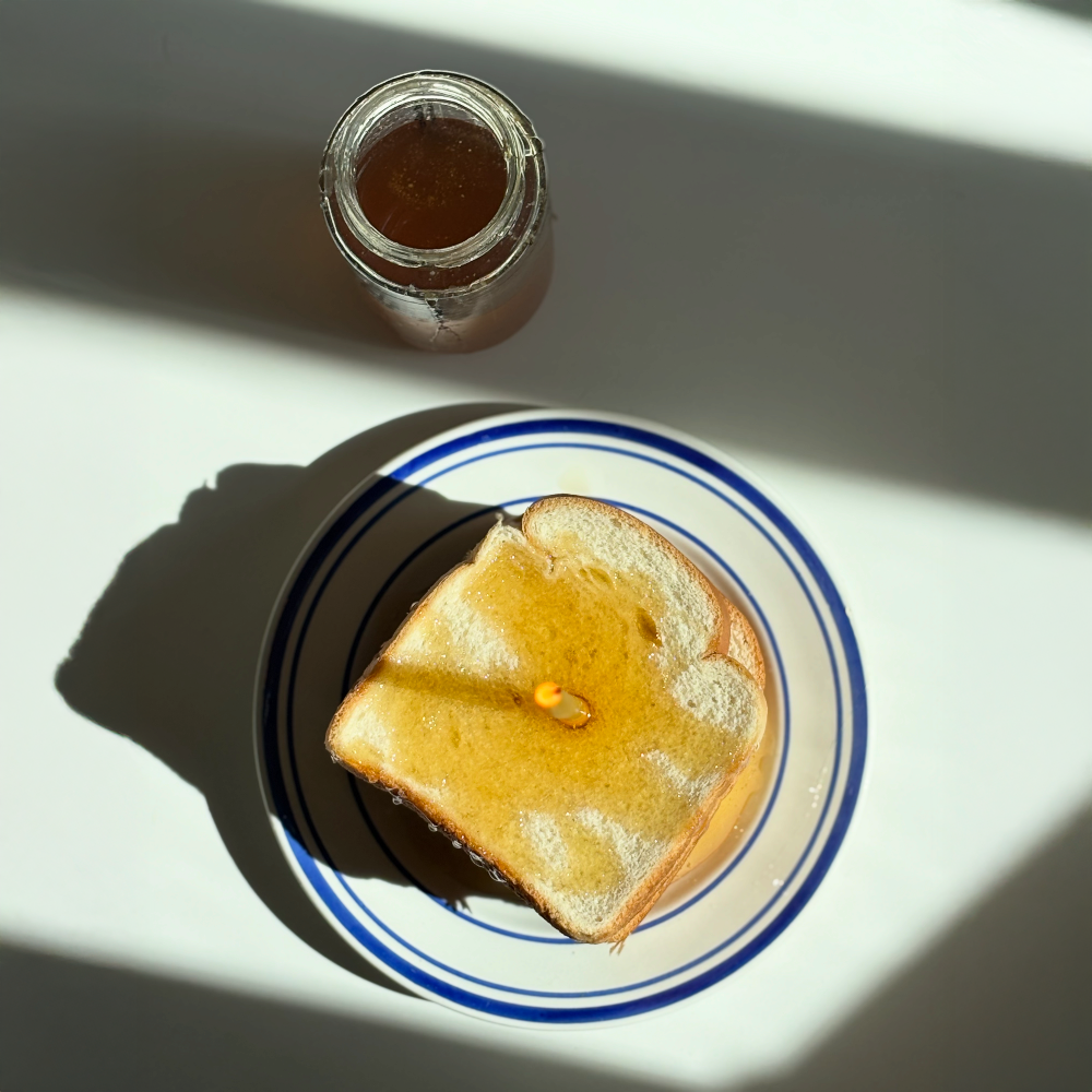 Toast with honey on a plate next to a jar of honey on a white surface.